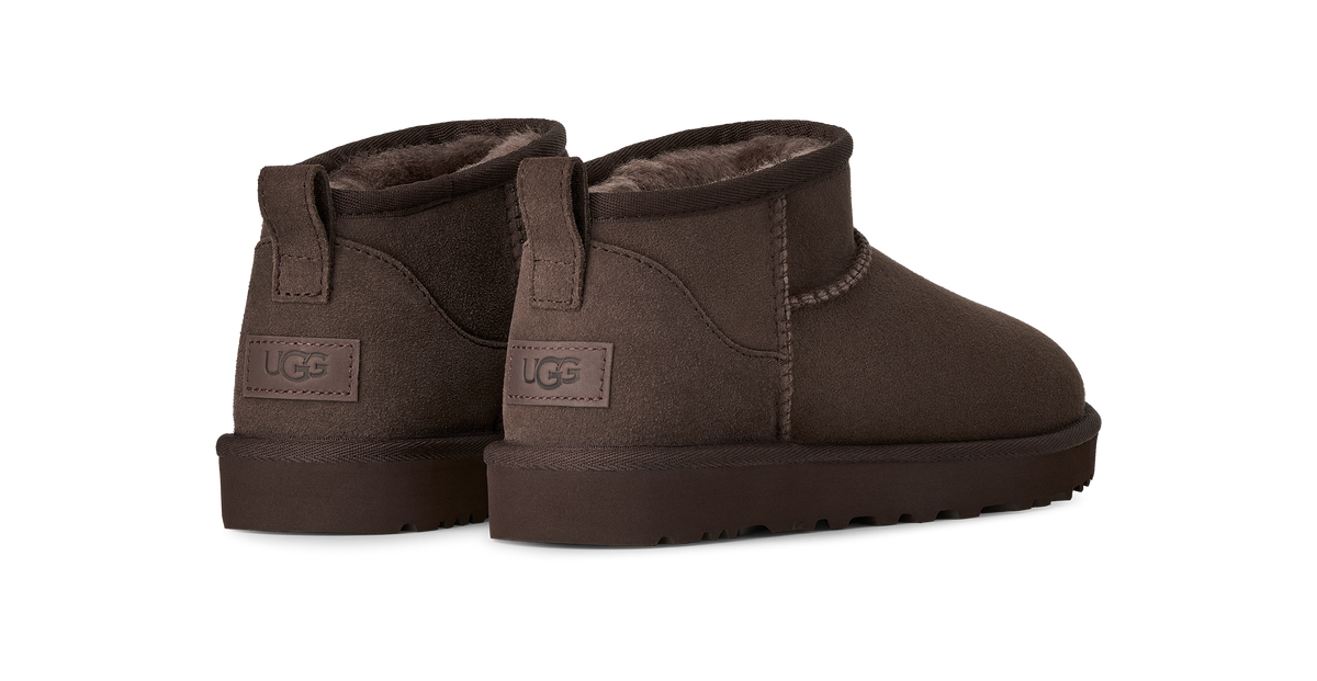 A pair of UGG mini ankle boots in dark brown suede with a soft brown faux-fur lining, shown from a three-quarters rear angle on a plain white background.