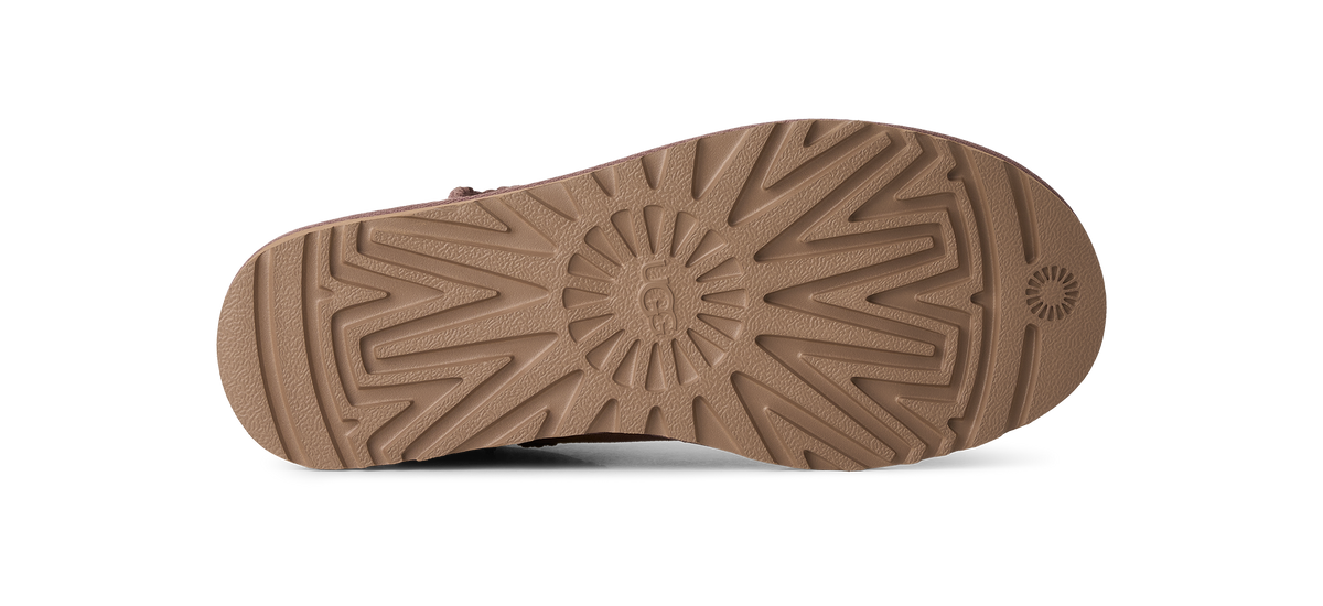 The bottom sole of a brown shoe, showing a detailed tread pattern and a circular logo embossed in the center, photographed on a clean white background.