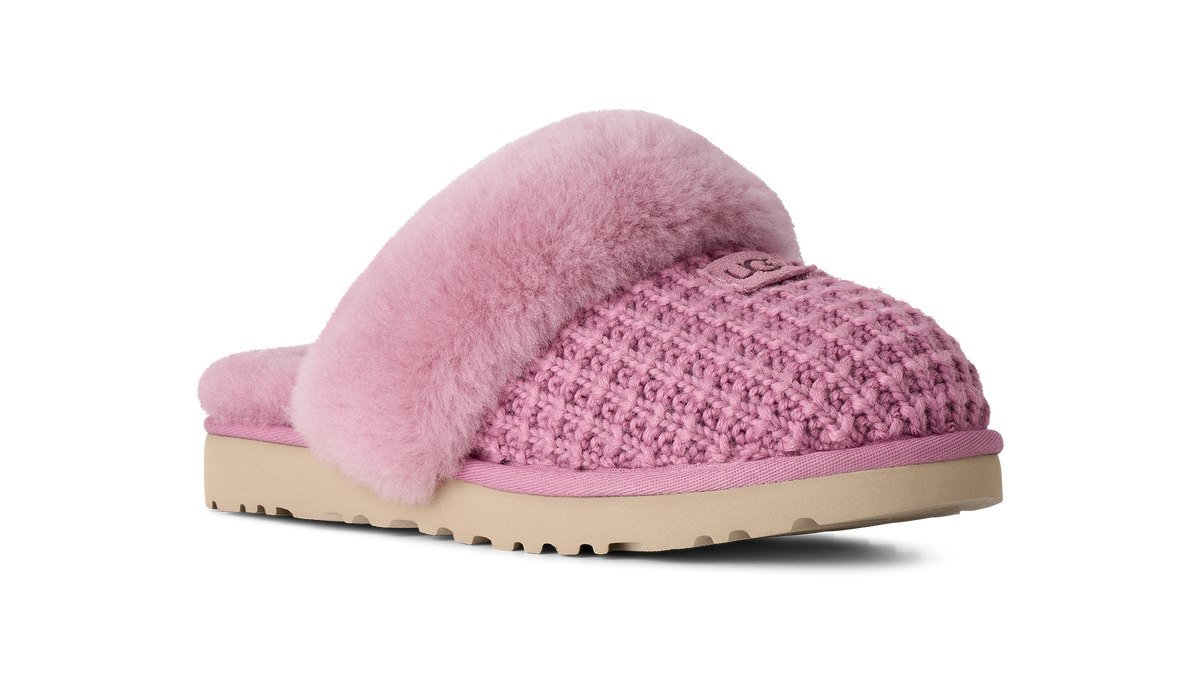 A pink knit slipper with fluffy pink faux-fur trim and a beige sole, shown from a side profile on a white background.