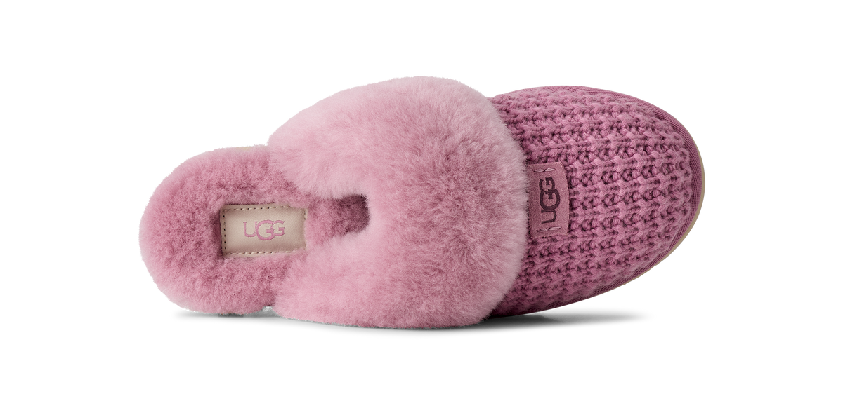 A single UGG slipper shown from the side on a white background, featuring a pink fuzzy shearling collar, a textured knit upper in a dusty mauve-pink, and a beige UGG logo patch on the heel.