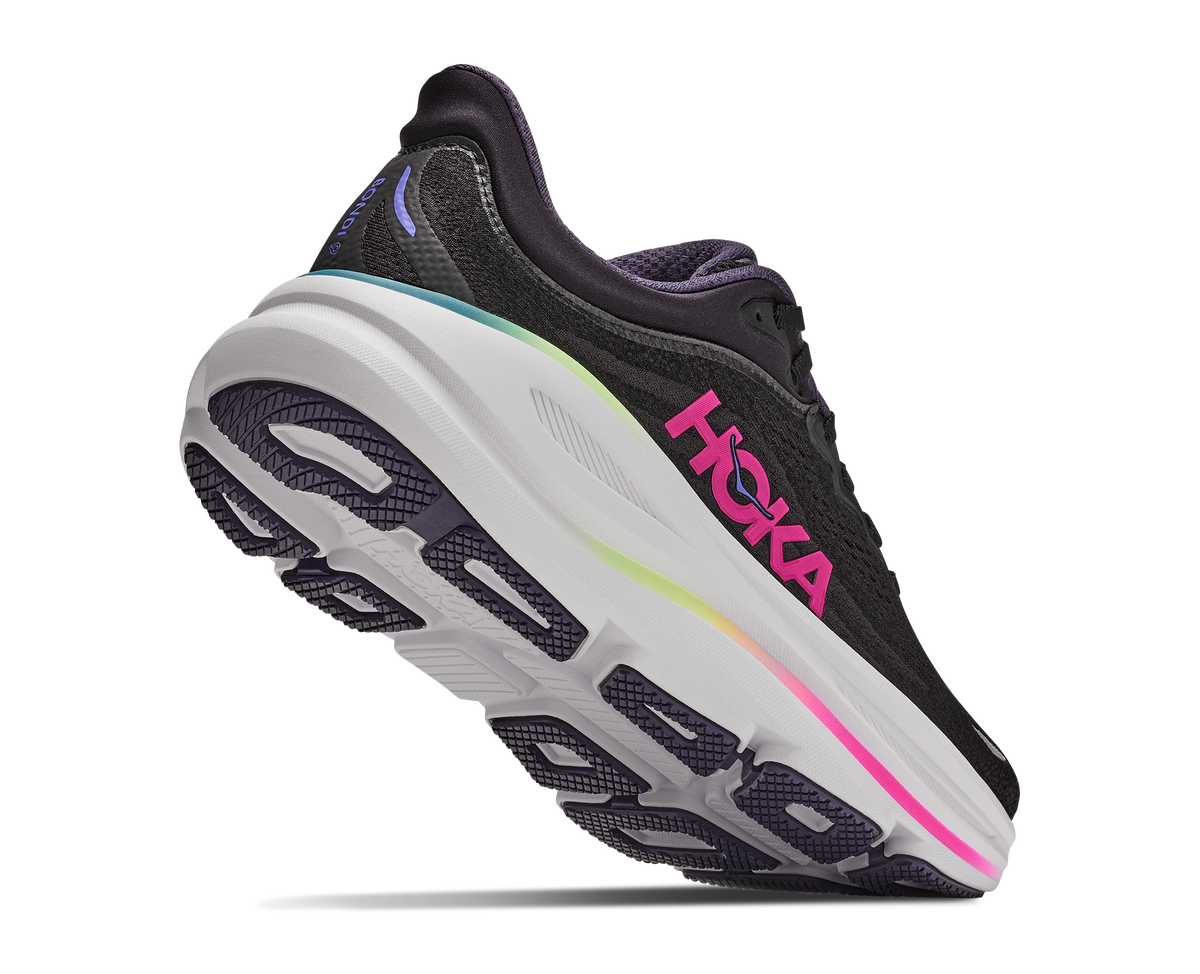 A Hoka running shoe in black and purple with a thick white midsole and a vibrant pink Hoka logo on the side, shown against a plain white background.