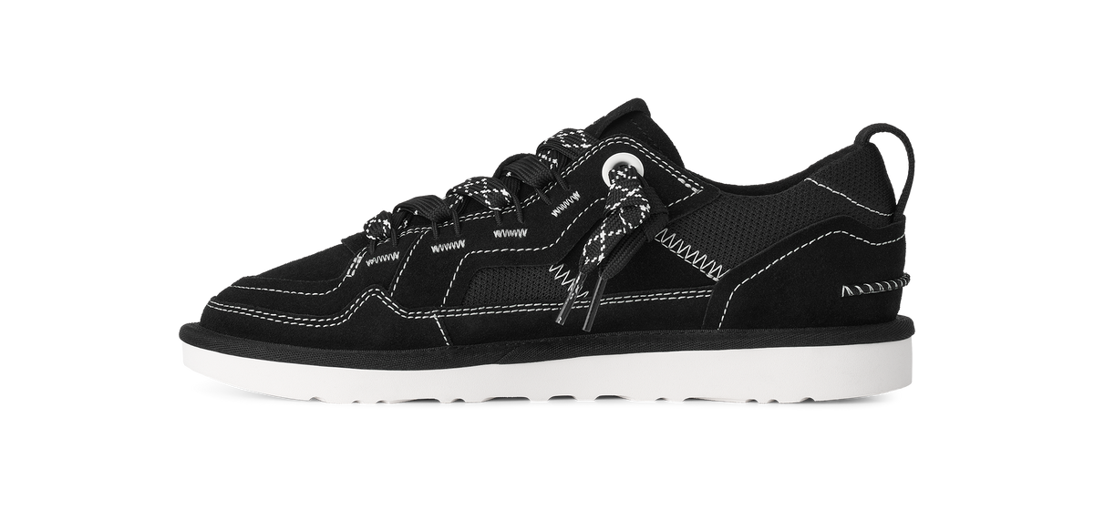 A black low-top sneaker with white contrast stitching, white laces, and a white sole, shown in a side profile on a white background.