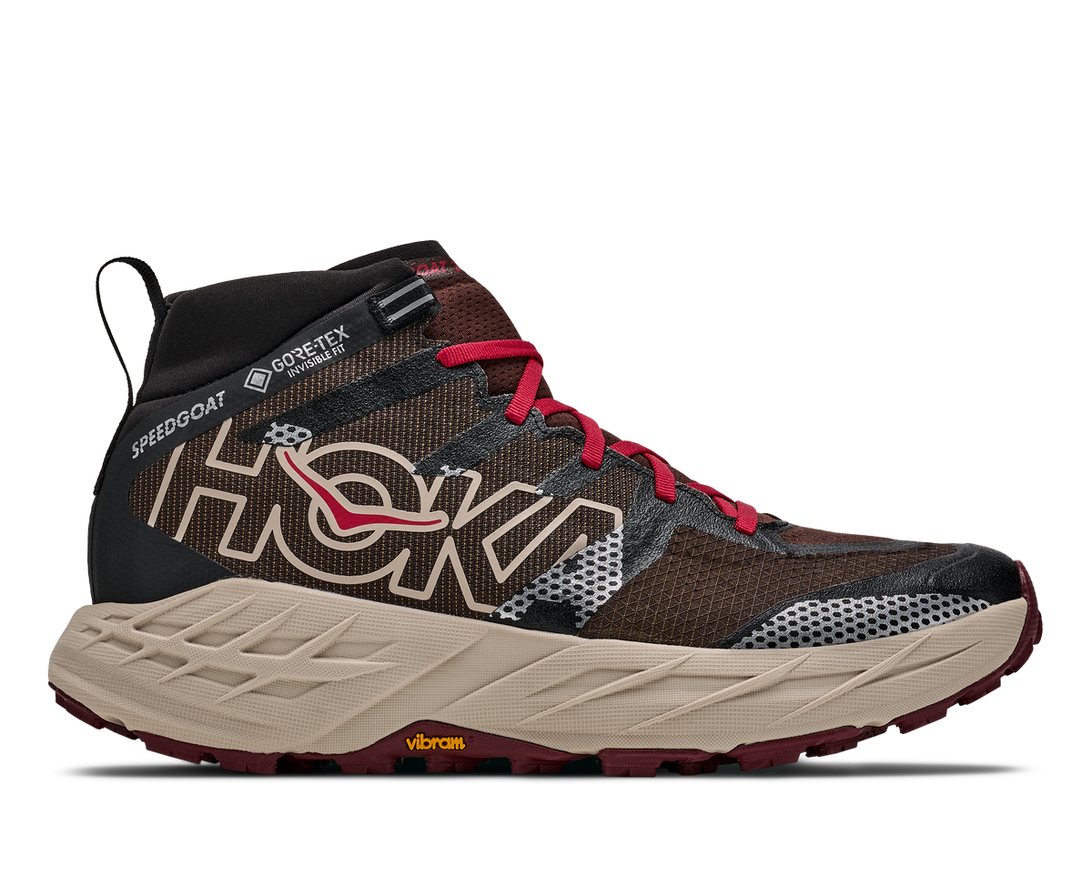 A Hoka mid-top trail running shoe in brown and black with red laces, a beige midsole, and a dark red outsole, shown from the side on a white background.
