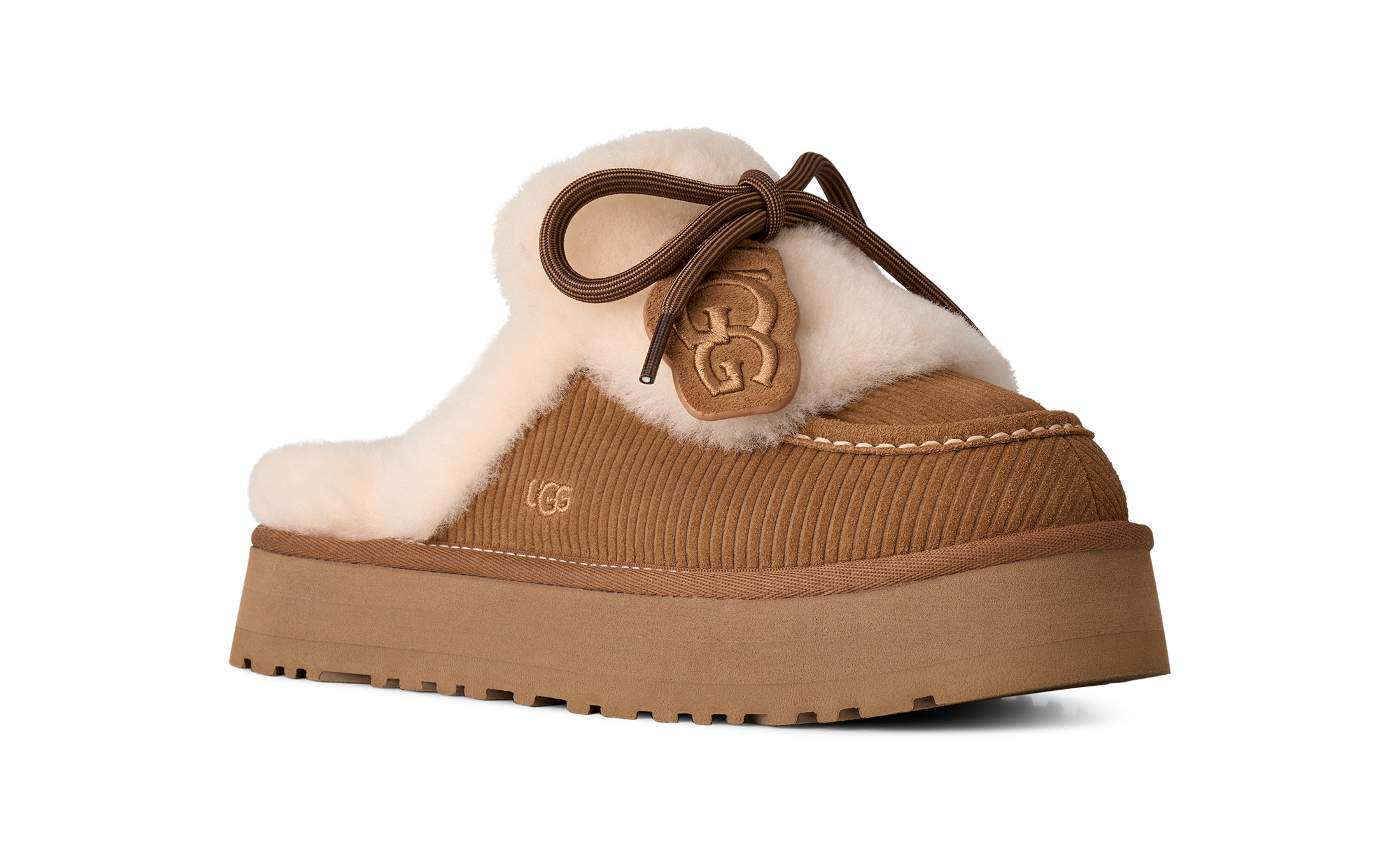 A single UGG slip-on mule slipper in tan suede with a thick platform sole, cream shearling lining, and a brown lace-up bow with a UGG logo charm, shown on a plain white background.