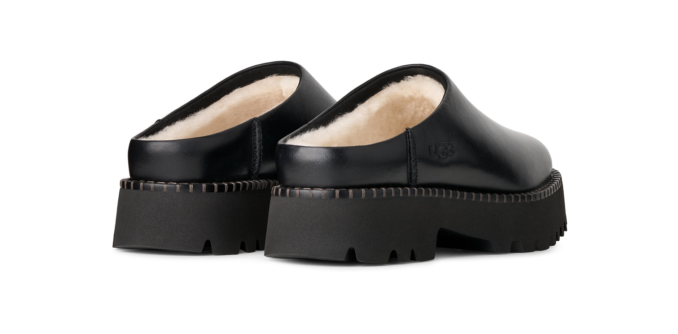 A pair of black leather UGG clogs with a cream shearling lining and chunky lug soles, shown from a rear three-quarter angle on a white background.