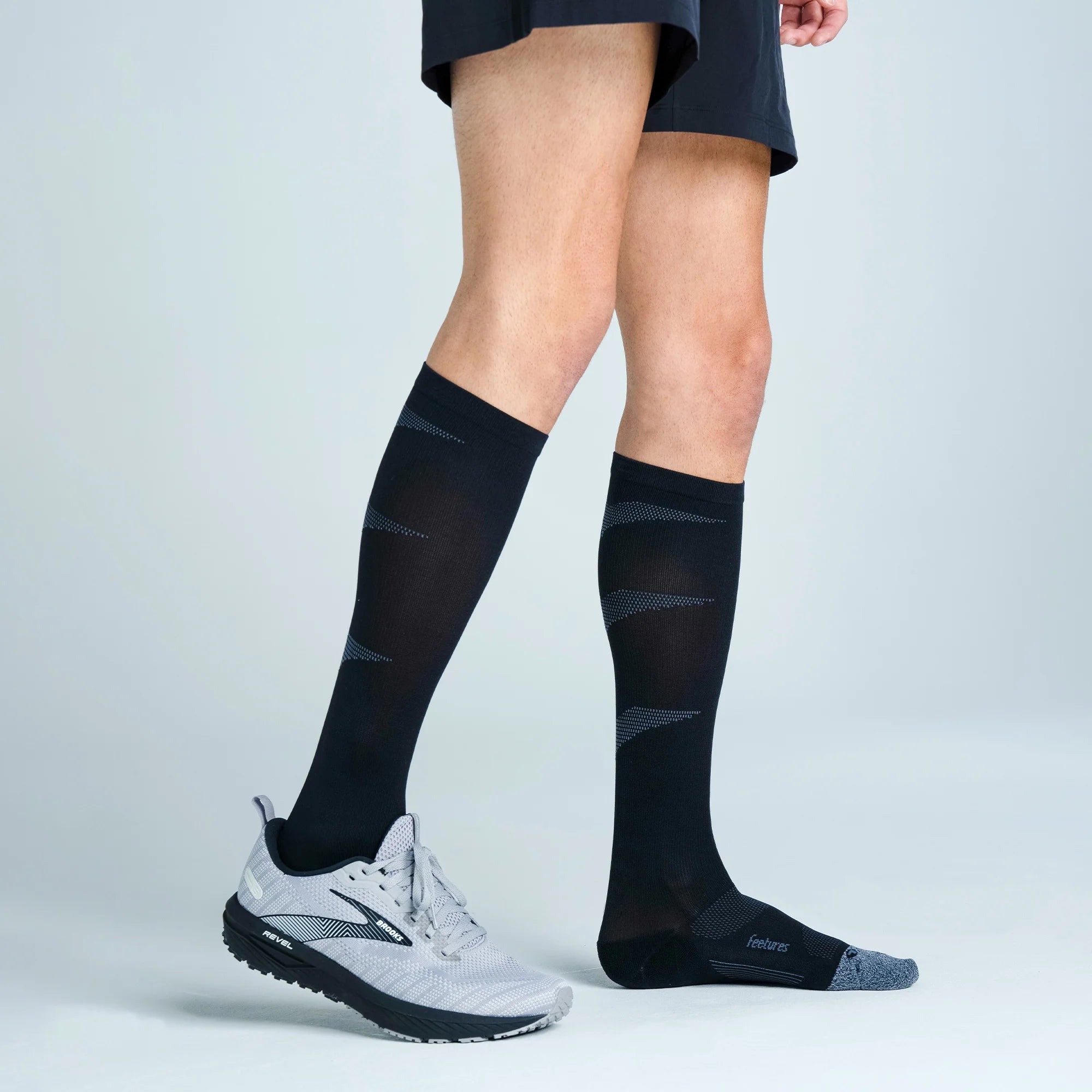 Person wearing black knee-high socks with a subtle pattern on a light gray background