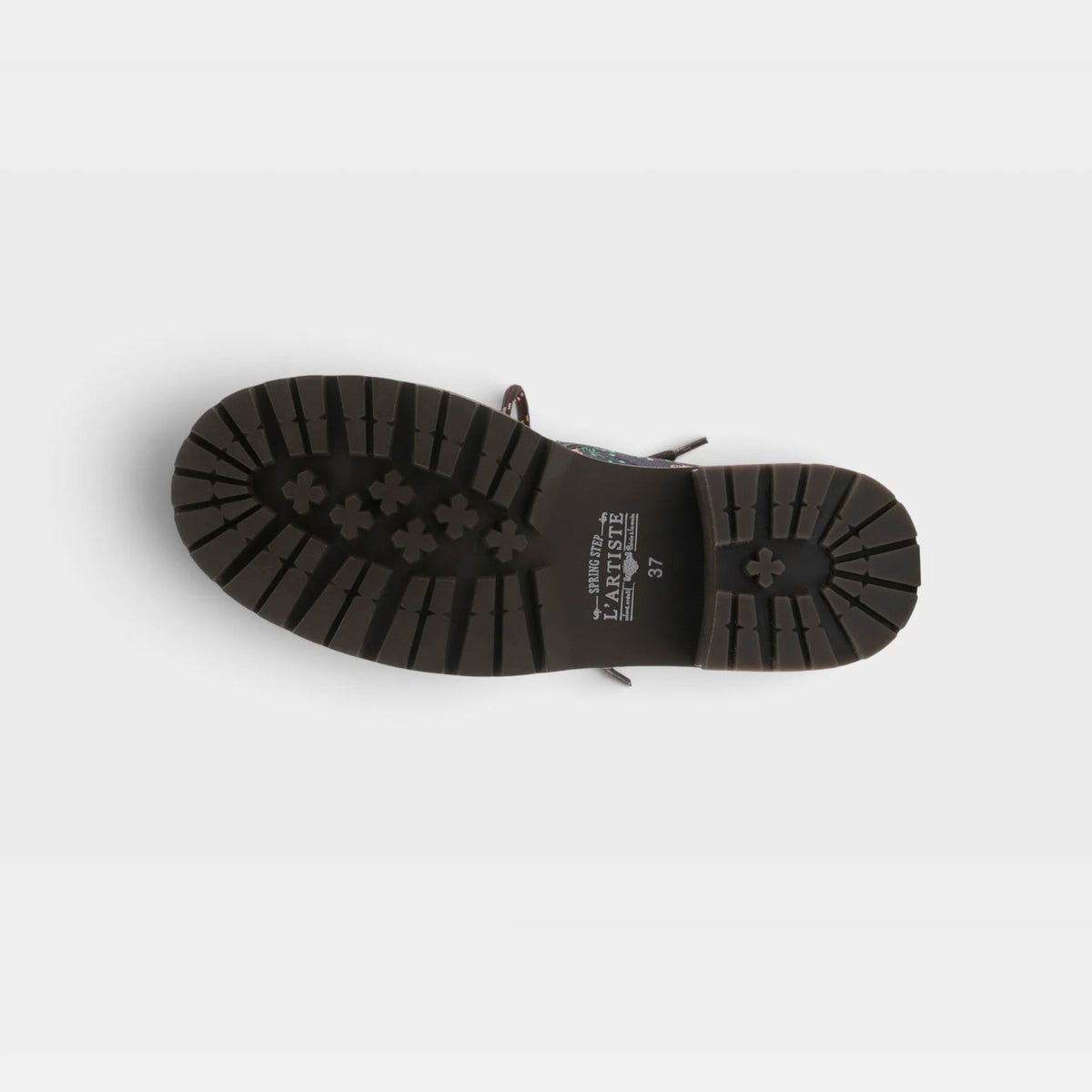 Top-down view of a black rubber shoe sole with a textured tread pattern and small white printed text in the center, shown on a light gray background.