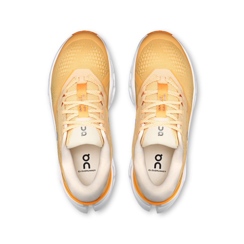 A top-down view of a pair of On Cloudrunner sneakers in a warm yellow and orange colorway, featuring a textured mesh upper, matching yellow-orange laces, and a white midsole.