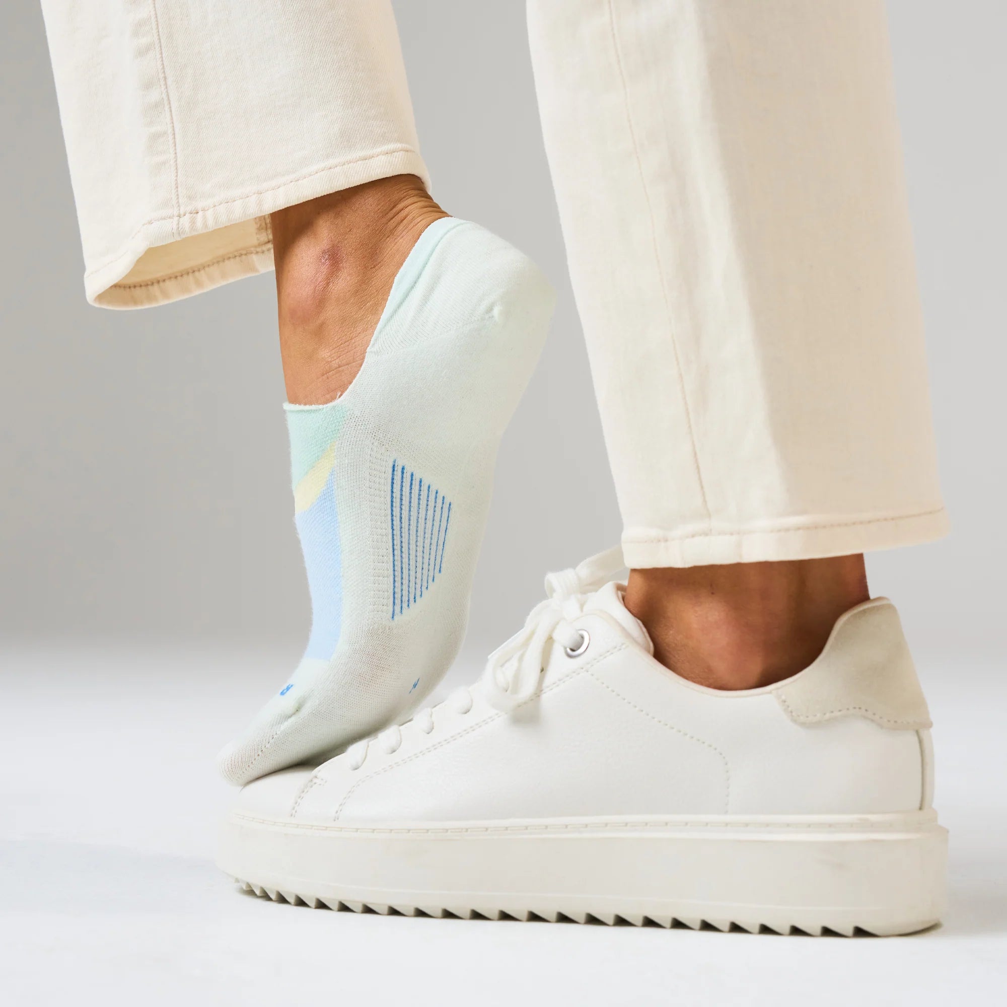 White sneakers worn with light-colored pants on a neutral background