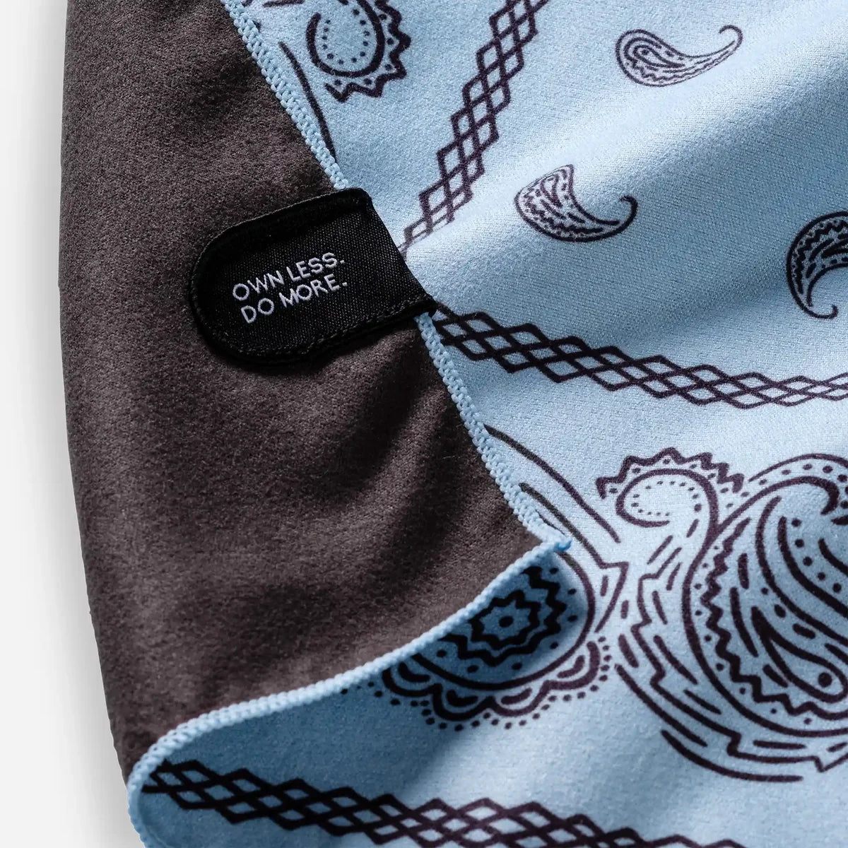 Blue bandana with black paisley patterns and a black tag with text on a white background