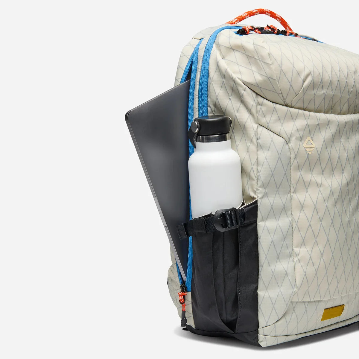 A close-up side view of a light beige backpack with a subtle diamond pattern, bright blue zippers, a black side pocket holding a white bottle and a dark laptop, and an orange top handle, set against a plain white background.