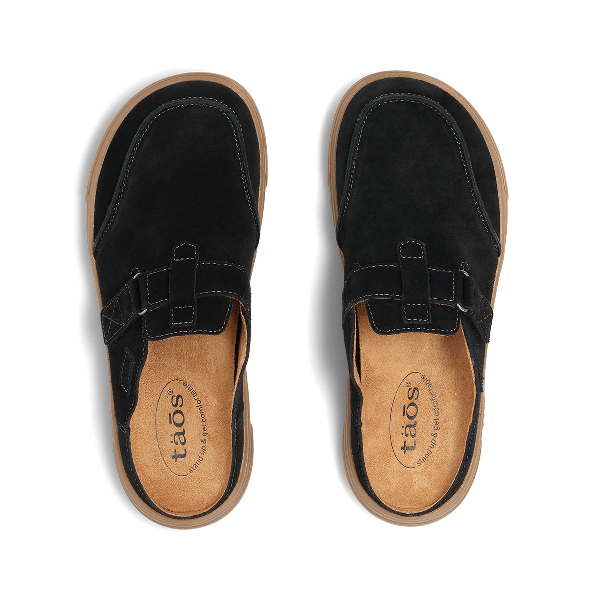 A pair of black suede mule sandals shown from a top-down view on a white background. The sandals feature a black strap with a silver buckle and a tan insole with the brand name 'taos' printed on it.
