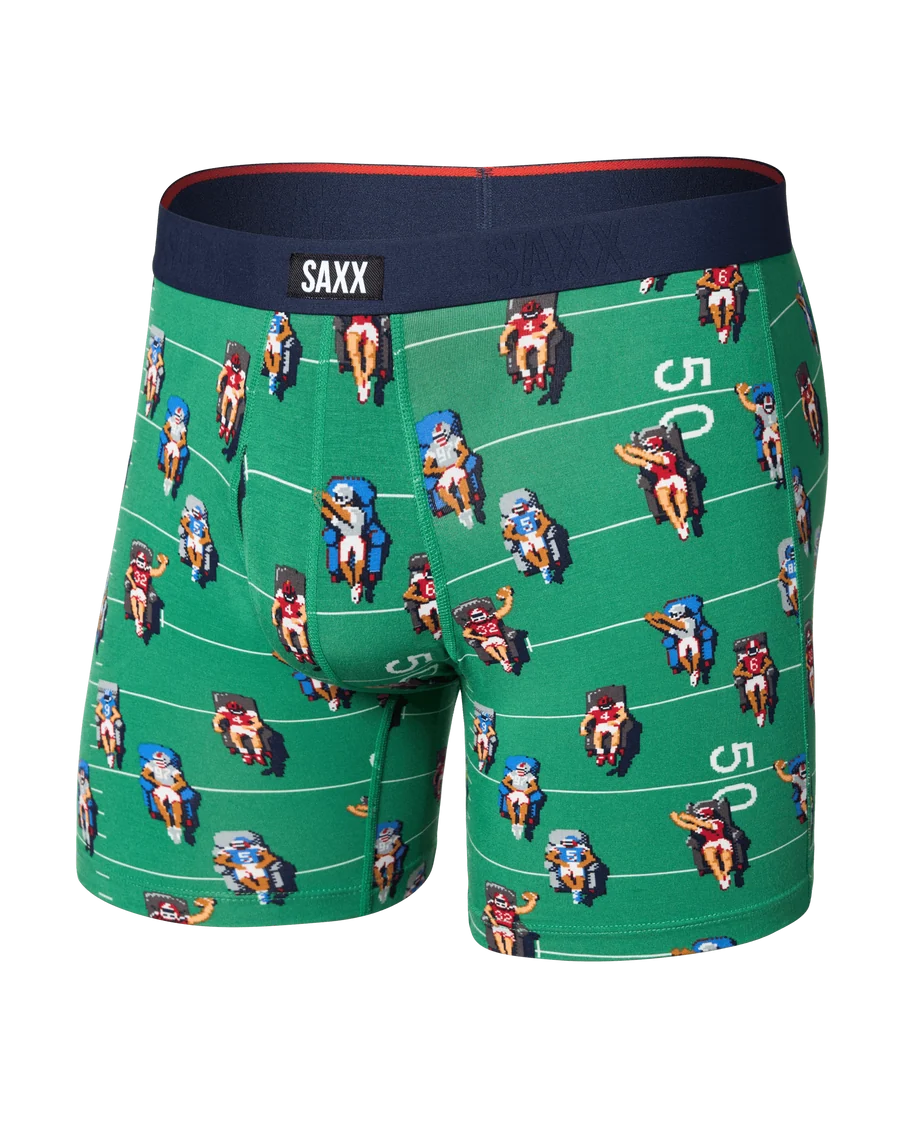 Green boxer briefs with a repeating football player pattern on a field background, featuring a navy blue waistband with the SAXX brand label.