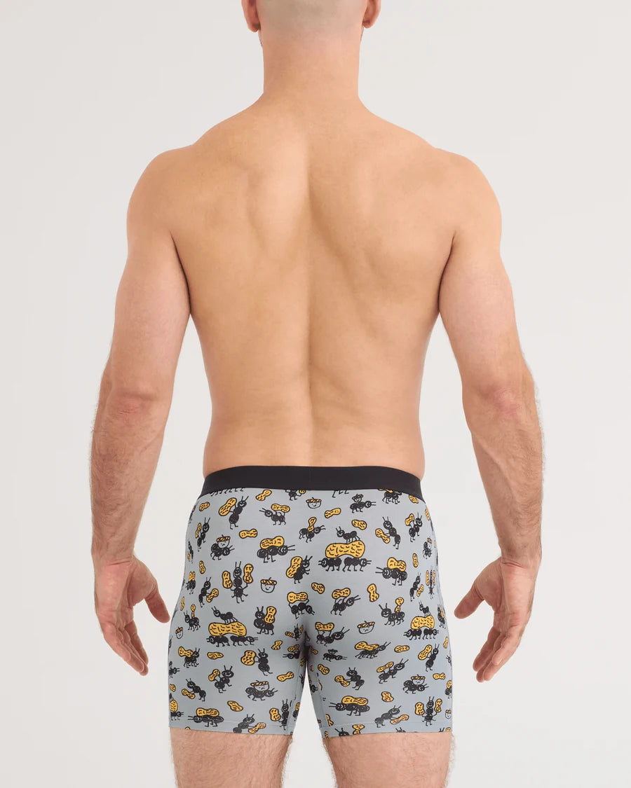 Rear view of a shirtless man wearing boxer briefs with a light gray background and a yellow and black animal print, against a plain light gray studio backdrop.