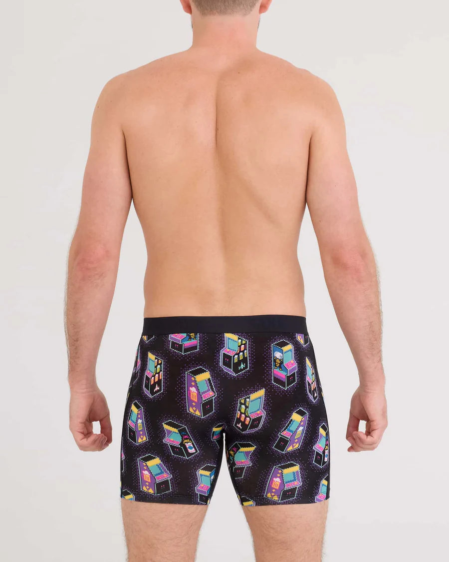 Man wearing black swim trunks with colorful claw machine pattern on a plain background