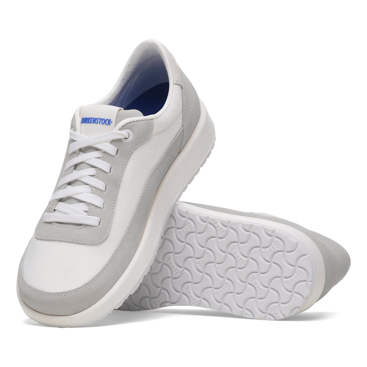 A pair of white and light gray low-top sneakers, with one shoe standing upright and the other lying on its side to show the textured sole, on a white background.