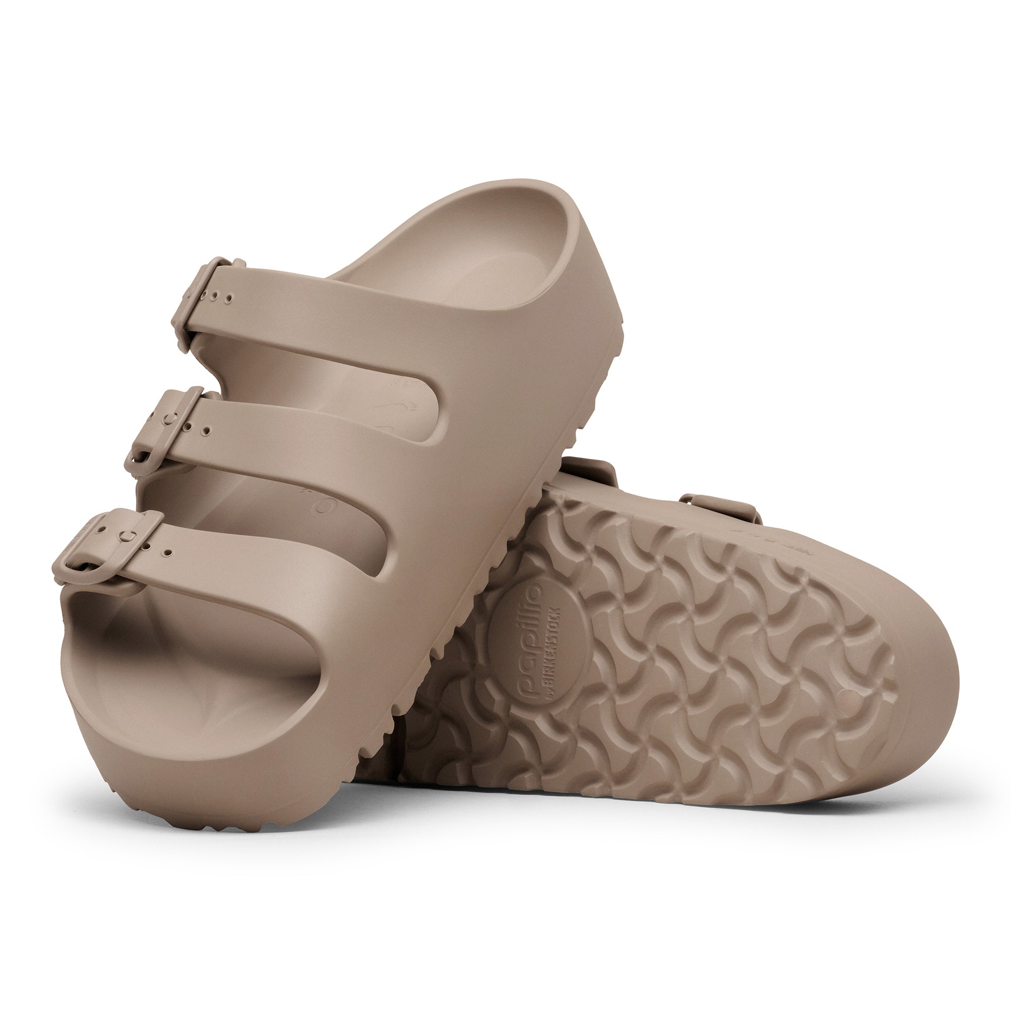 Pair of beige sandals with a textured sole on a white background