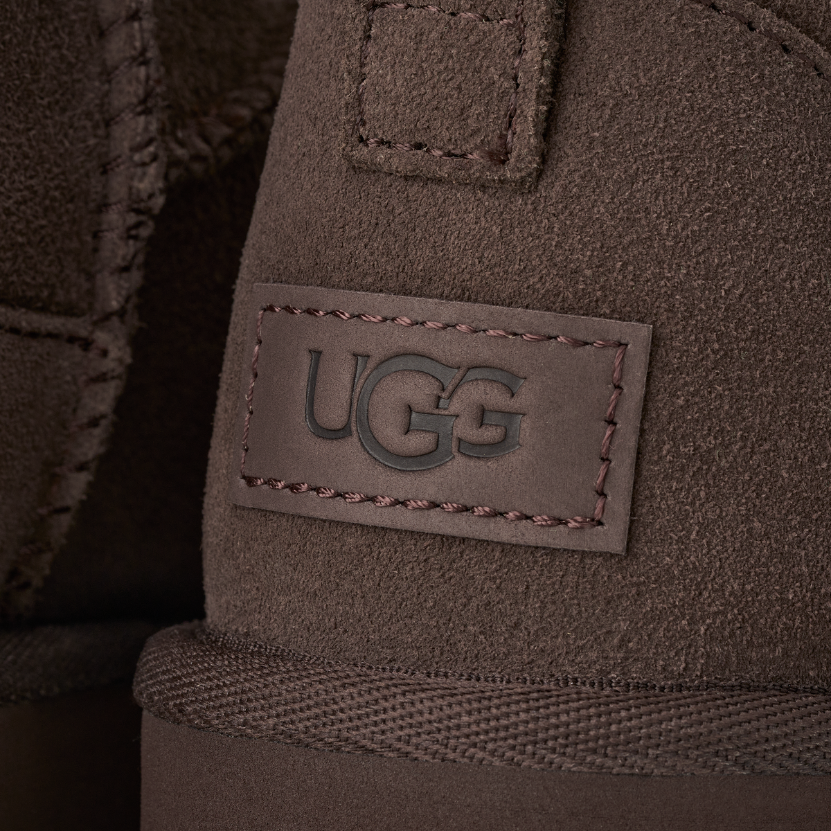 Close-up of a brown suede UGG boot with a stitched rectangular logo patch on the side.
