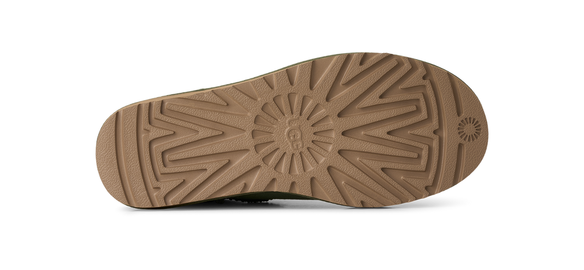 The bottom sole of a shoe, showing a tan rubber tread pattern with a central sunburst design and a small circular logo on the heel, photographed against a white background.