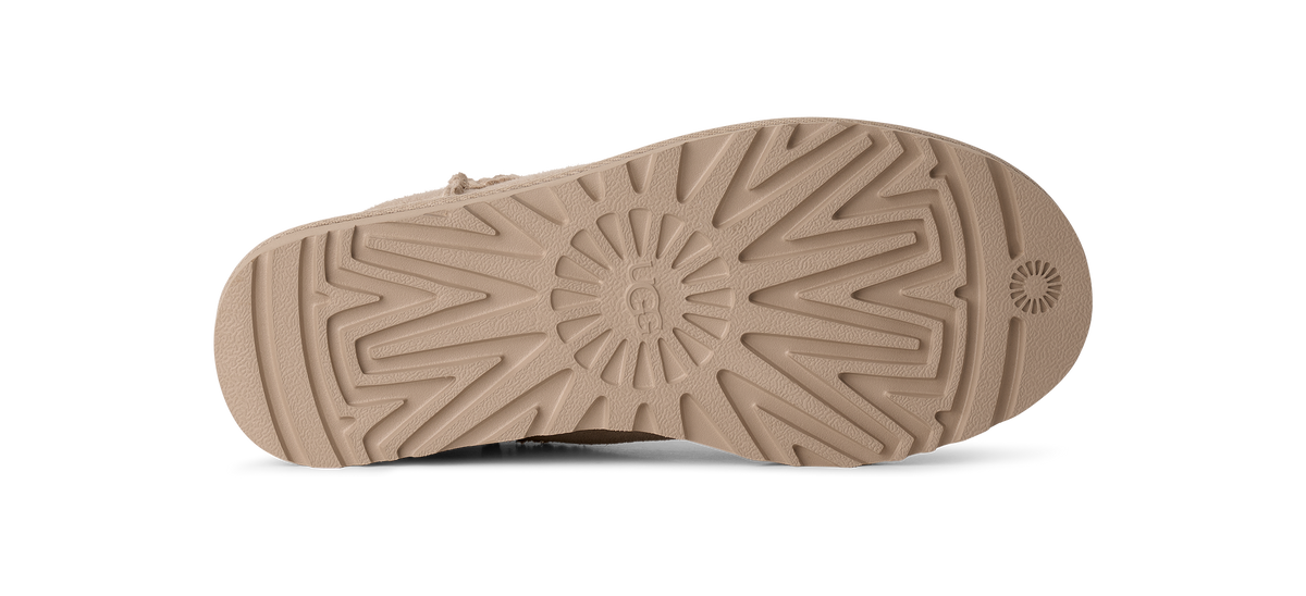 The bottom sole of a tan boot, showing a detailed tread pattern and a circular logo embossed near the heel, on a solid white background.