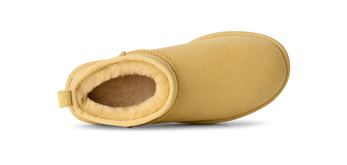 A single mustard yellow suede ankle boot with a soft tan shearling lining, shown from a side profile view on a white background.