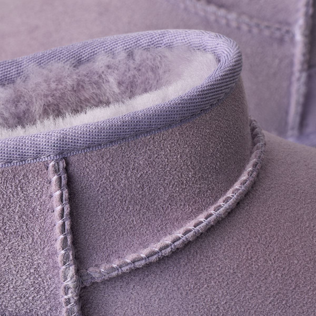 Close-up of a light purple suede boot with a soft white shearling lining and matching purple stitching.