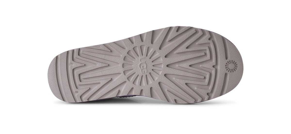The bottom sole of a shoe, showing a textured tread pattern and a circular logo embossed in the center, in a solid taupe-gray color against a white background.
