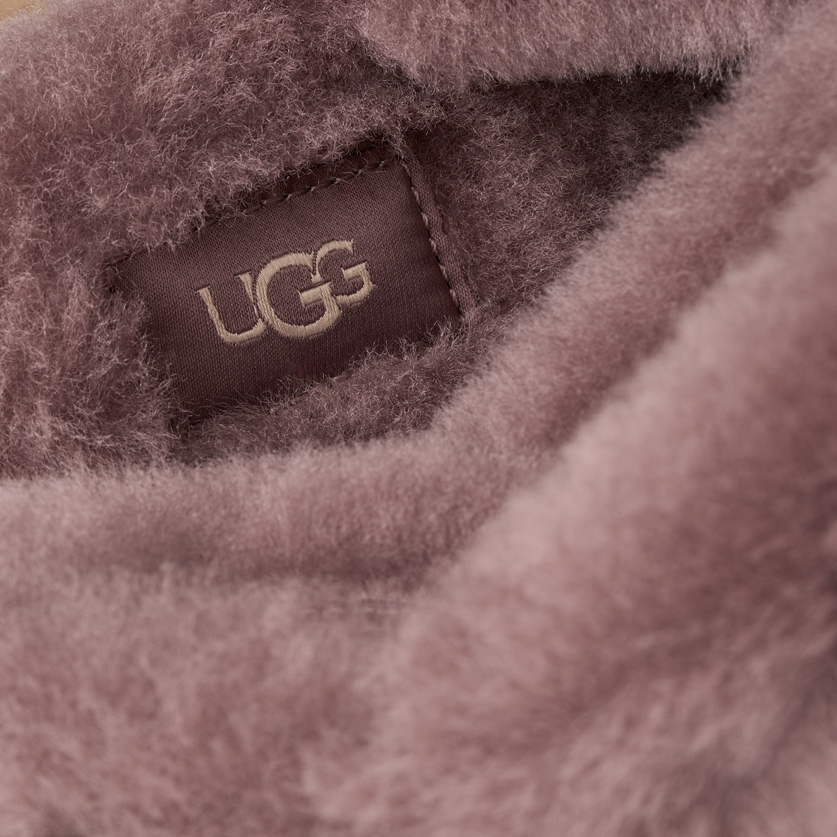 Close-up of a soft, fuzzy mauve-pink textile with a sewn-in UGG label visible in the center.