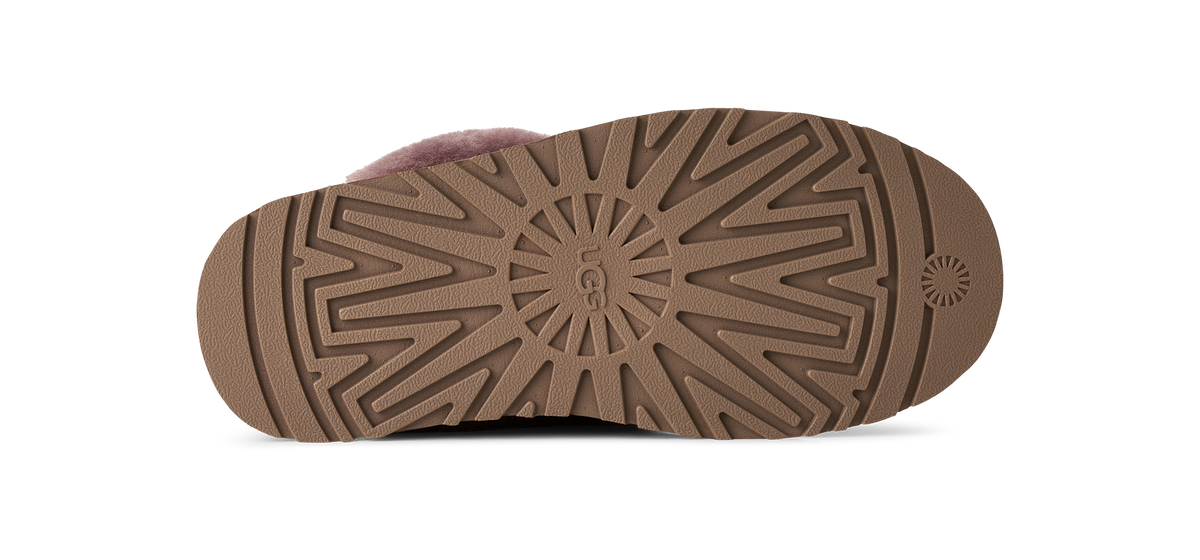 The bottom sole of a UGG slipper, showing a brown textured radial tread pattern with the embossed UGG logo in the center, photographed on a white background.