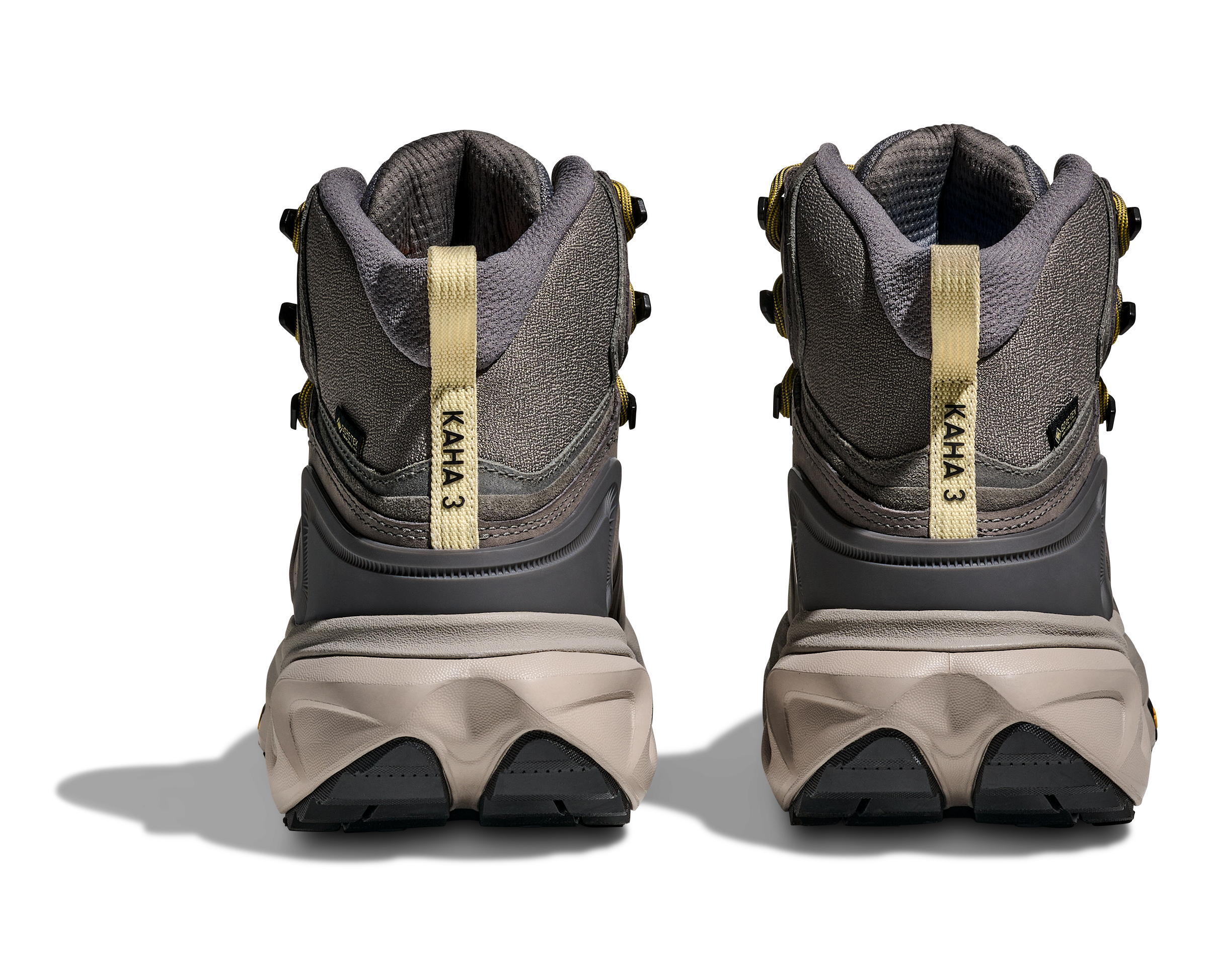 A pair of KAHA 3 mid-top hiking boots shown from the back, featuring a gray and dark gray upper with beige midsoles and gold-colored heel pull tabs.