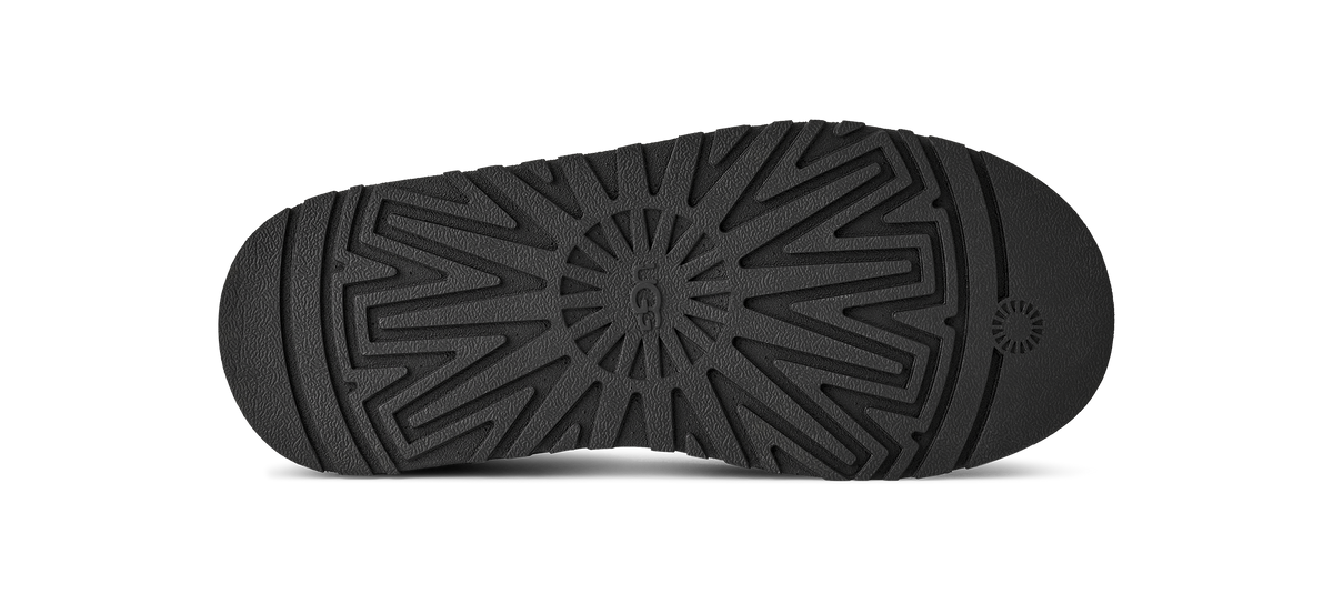 The black rubber outsole of a shoe, showing a detailed tread pattern and a circular logo on the heel, isolated on a white background.
