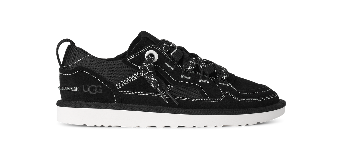 A black UGG sneaker with white contrast stitching, white laces, and a white sole, shown in a side profile on a white background.