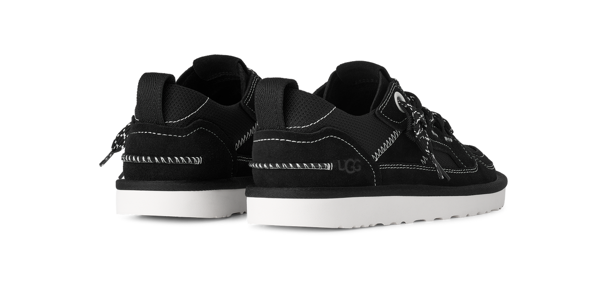 A pair of black low-top sneakers with white stitching, white soles, and black-and-white laces, shown from a three-quarters angle on a white background.