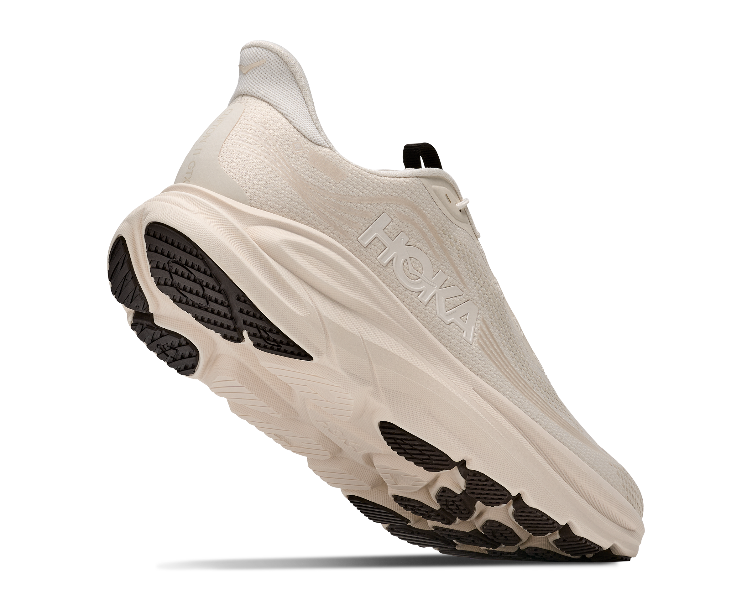 A single HOKA running shoe shown from a side angle against a solid white background. The shoe features a cream-colored mesh upper, a thick cream midsole, and a black textured outsole.