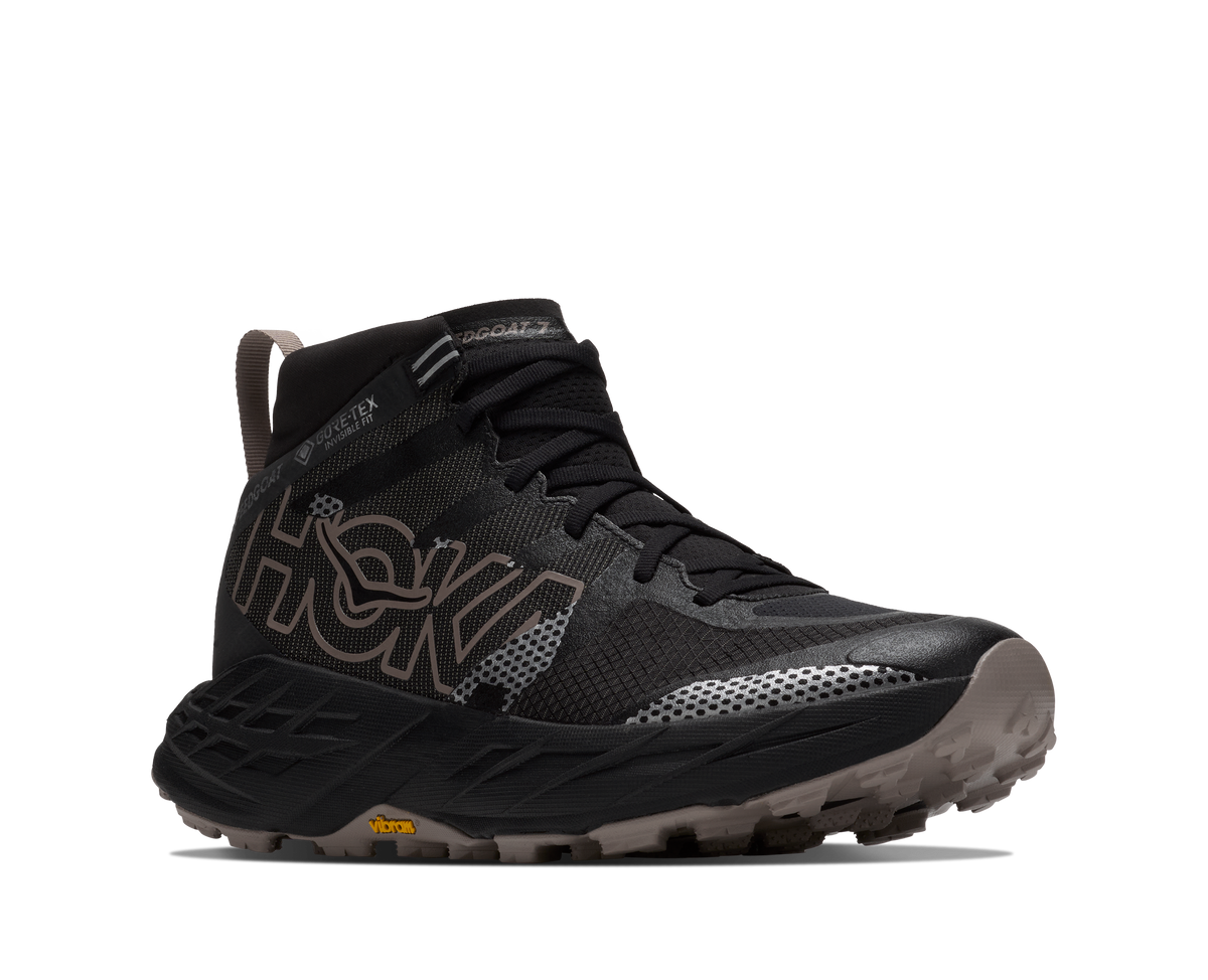 A black HOKA trail running boot with brown and gray accents, featuring a lace-up front, ankle support, and a rugged sole, shown against a plain white background.