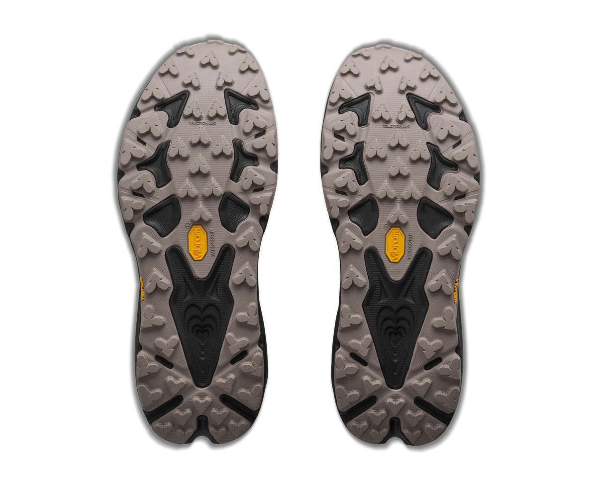 A pair of hiking shoe soles shown from above on a plain white background, featuring a rugged gray and black tread pattern with small yellow Vibram logos near the center of each sole.
