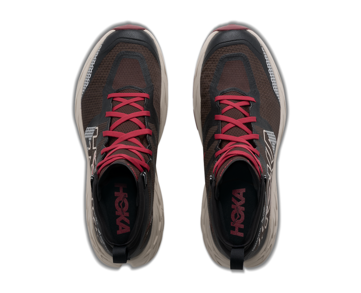 A pair of HOKA running shoes shown from a top-down view, featuring a dark brown and black mesh upper with vibrant pink laces and a thick, chunky off-white sole.