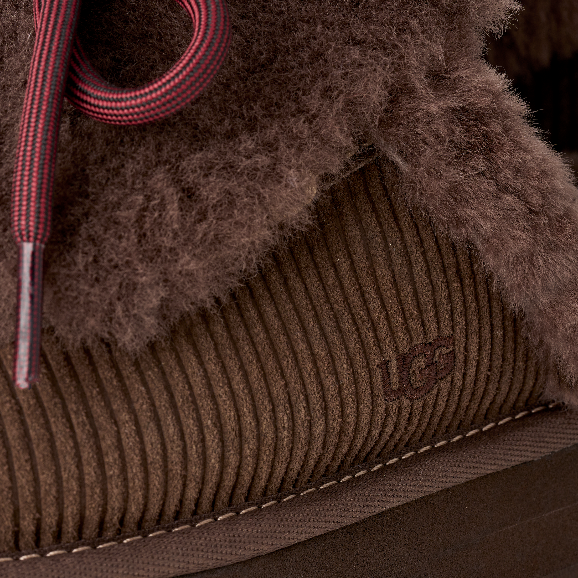 Close-up of a brown corduroy shoe with fur lining and red laces.