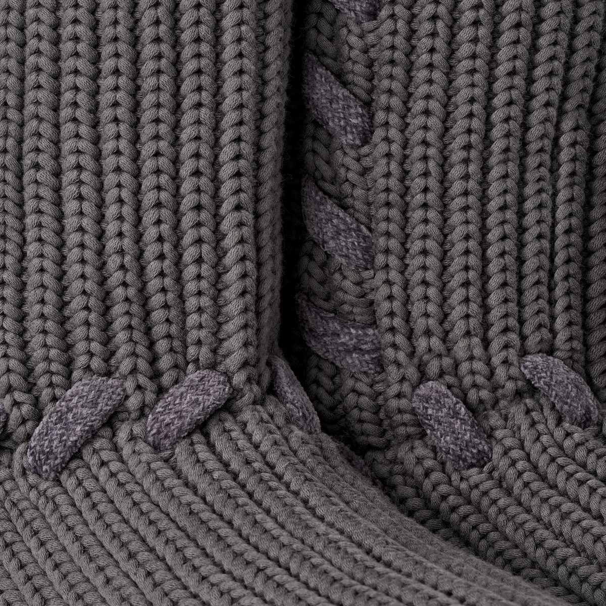 Close-up of a chunky knit garment in dark gray, showing ribbed texture and contrasting knotted tie details.