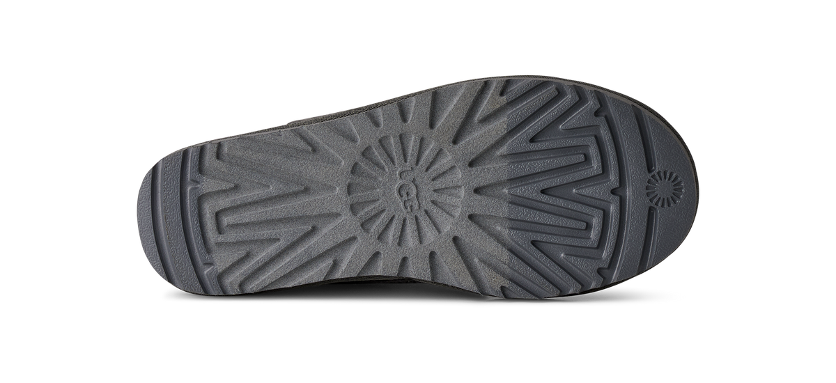 The bottom sole of a brown boot, showing a detailed tread pattern and a circular embossed logo on a white background.