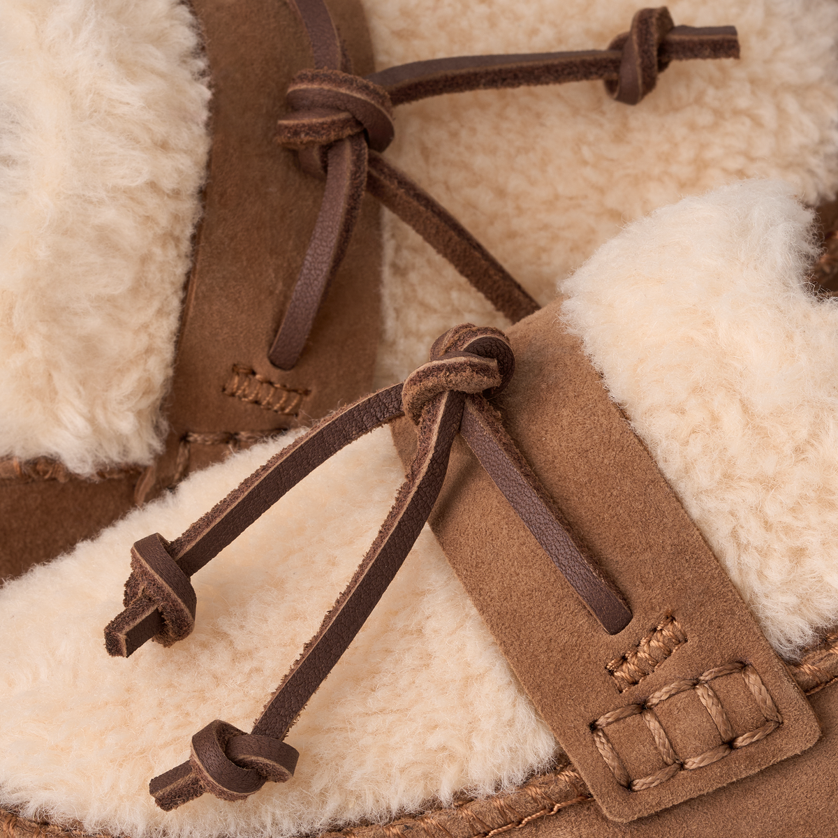 Close-up of brown suede moccasin-style slippers with thick cream shearling lining and dark brown drawstring ties.