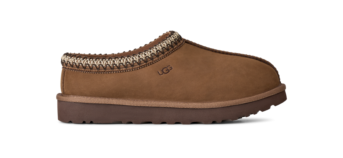 A single brown suede slipper shoe with a braided trim and a brown sole, shown in profile against a white background. The embossed logo on the side reads UGG.