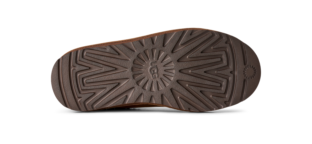 A close-up view of a brown rubber shoe sole with a textured tread pattern and a circular logo embossed in the center, shown against a plain white background.