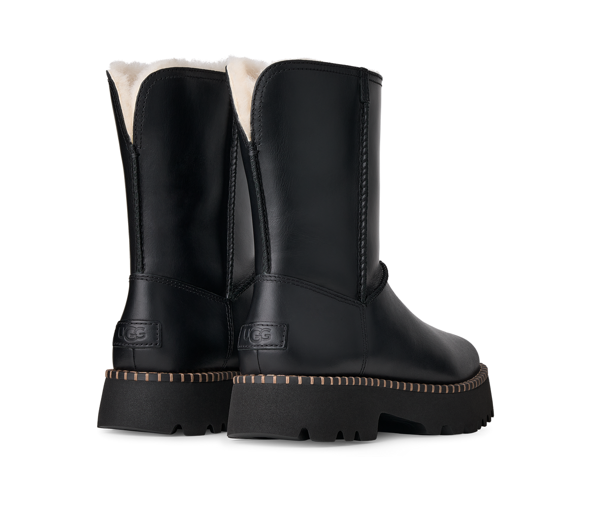 A pair of black UGG ankle boots with a soft cream shearling lining visible at the top and a chunky black sole with tan contrast stitching, shown from a three-quarter angle on a white background.