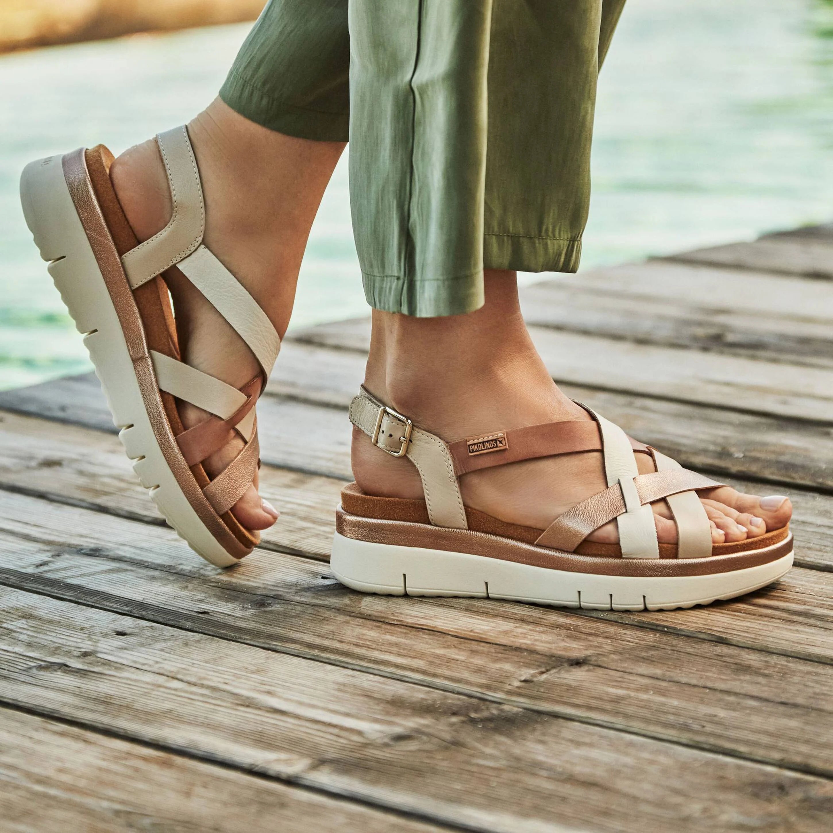 Beige sandals worn on a wooden deck with a blurred natural background
