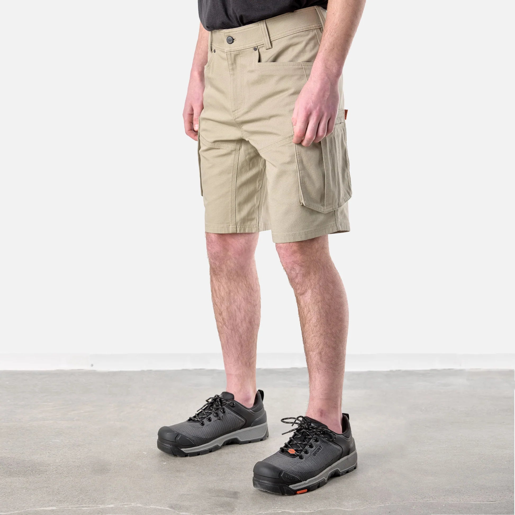 Person wearing beige shorts and black hiking shoes on a light gray floor.