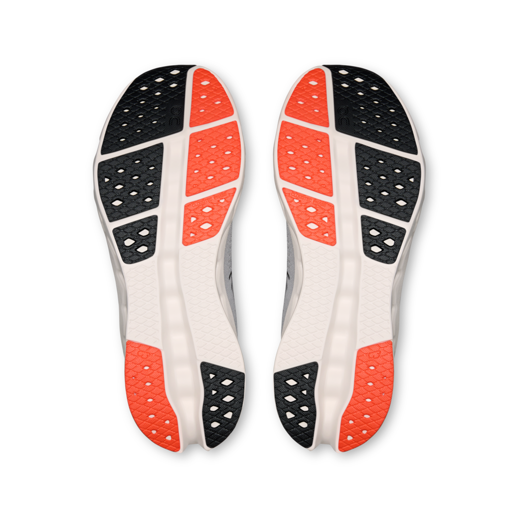 A pair of athletic shoes shown from the sole view, featuring a white midsole with black and bright orange textured grip patterns, set against a plain white background.