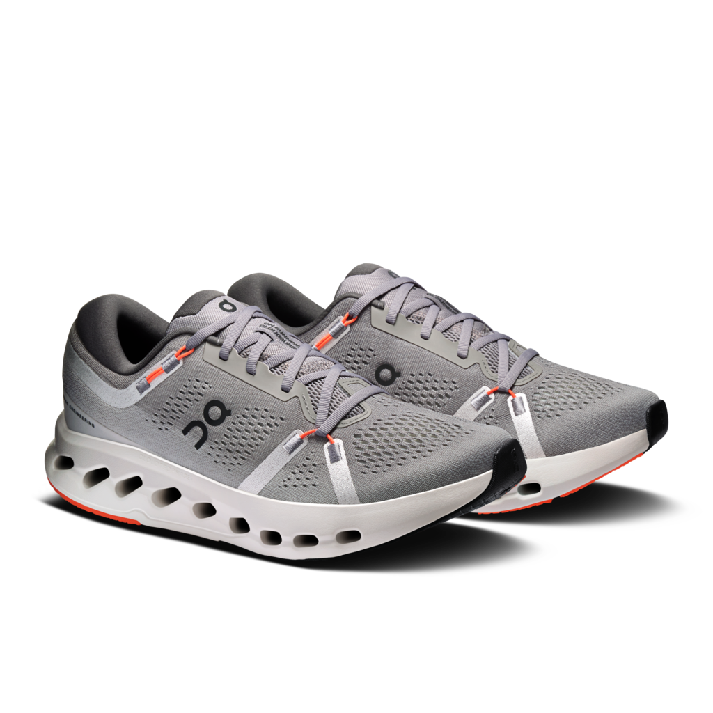 A pair of On running shoes in gray, featuring a breathable mesh upper, a thick cushioned sole with visible air pockets, and small orange accents on the laces and outsole.