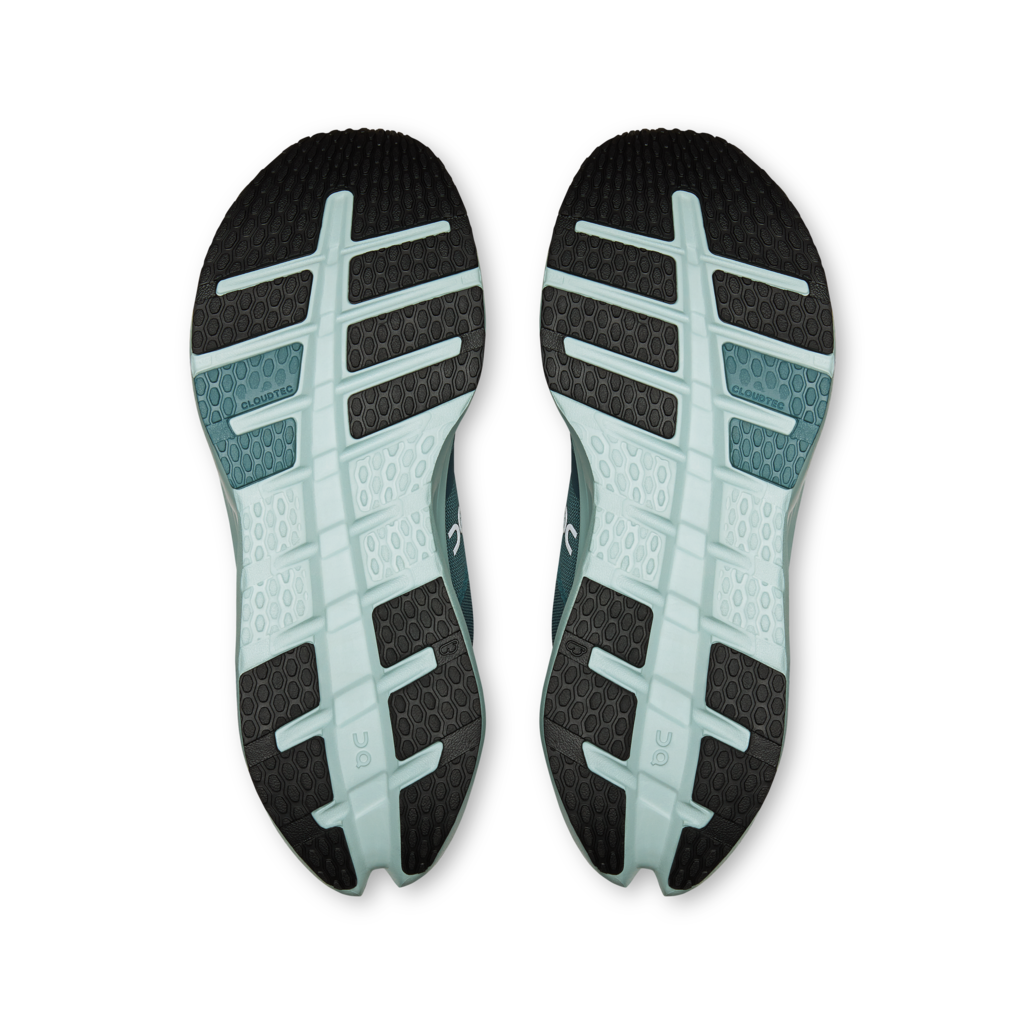 Top-down view of a pair of running shoes showing their textured black outsoles with a light teal and white segmented tread pattern, set against a plain white background.