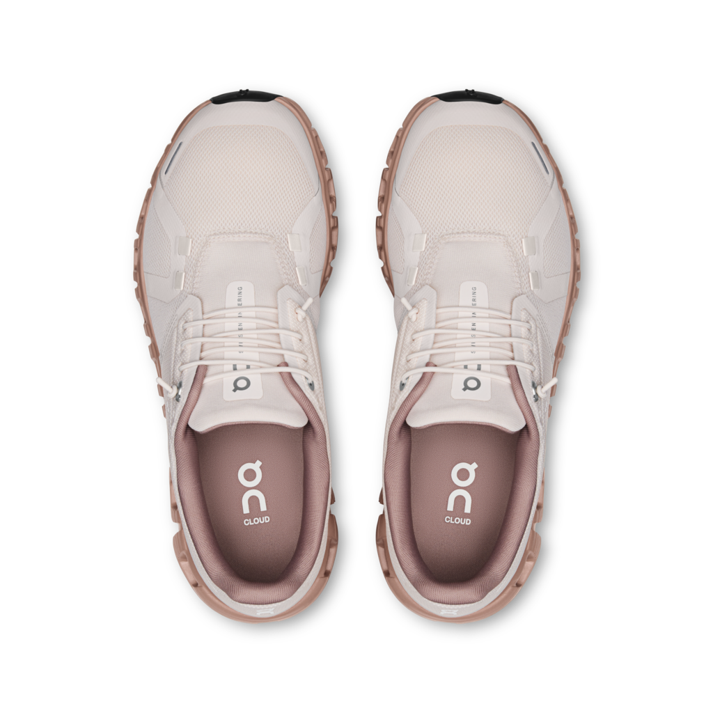 A pair of On Cloud running shoes shown from a top-down view, featuring a light beige mesh and synthetic upper with a dusty rose pink lining and a brown midsole.